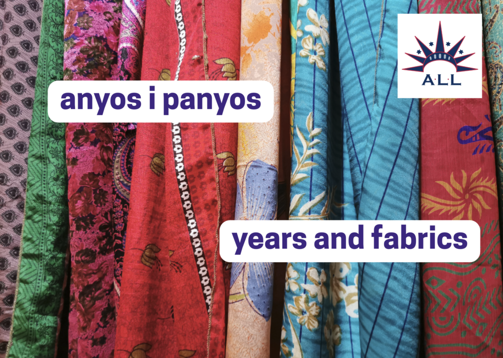 Colorful bolts of cloth with the words "Anyos i panyos" - "Years and Fabrics"